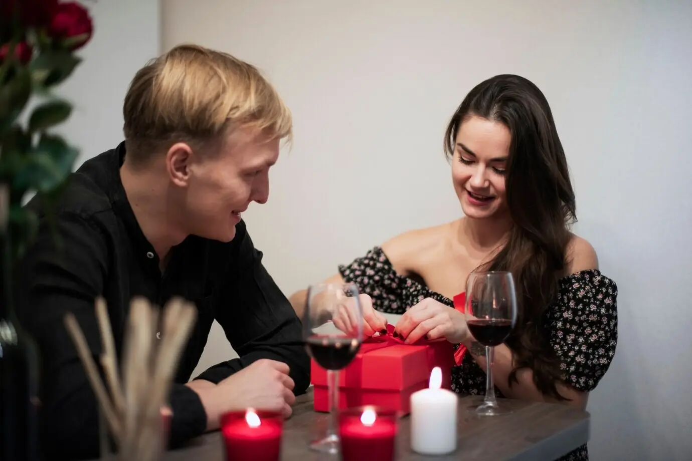 Couple romantique célébrant la Saint-Valentin à la maison avec du vin et un cadeau.
